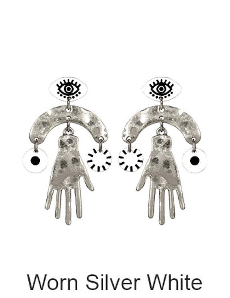 May include: Worn silver earrings with a white eye design, a hand shape, and a circle with black lines. The earrings are in the Worn Silver White color.