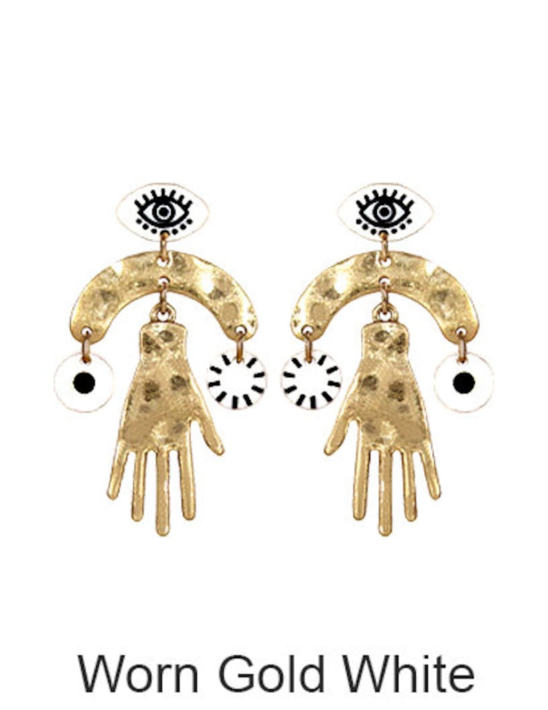 May include: A pair of gold-tone earrings with a white and black eye design, a hand-shaped charm, and a circle charm.