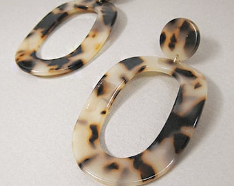 May include: A pair of oval-shaped earrings with a tortoiseshell pattern. The earrings are made of a white and brown plastic material.