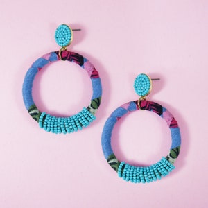 Pode incluir: Um par de brincos de argola azul e rosa com contas turquesa. Os brincos são feitos de tecido e têm um padrão floral.