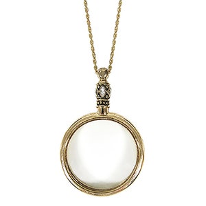 May include: Antique gold-colored magnifying glass pendant necklace. The pendant features a round magnifying glass with a decorative bezel and a small, ornate top with a clear stone. The chain is a delicate gold color. The text "Antique Gold" is below the pendant.