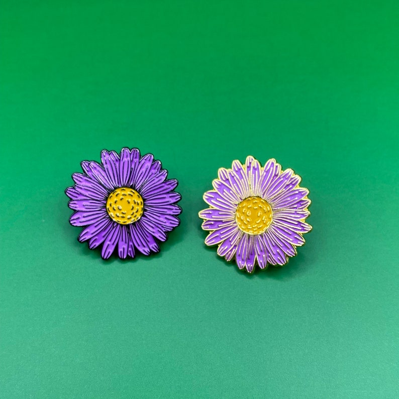 May include: Two purple and yellow enamel flower pins. The flowers have a yellow center and purple petals.