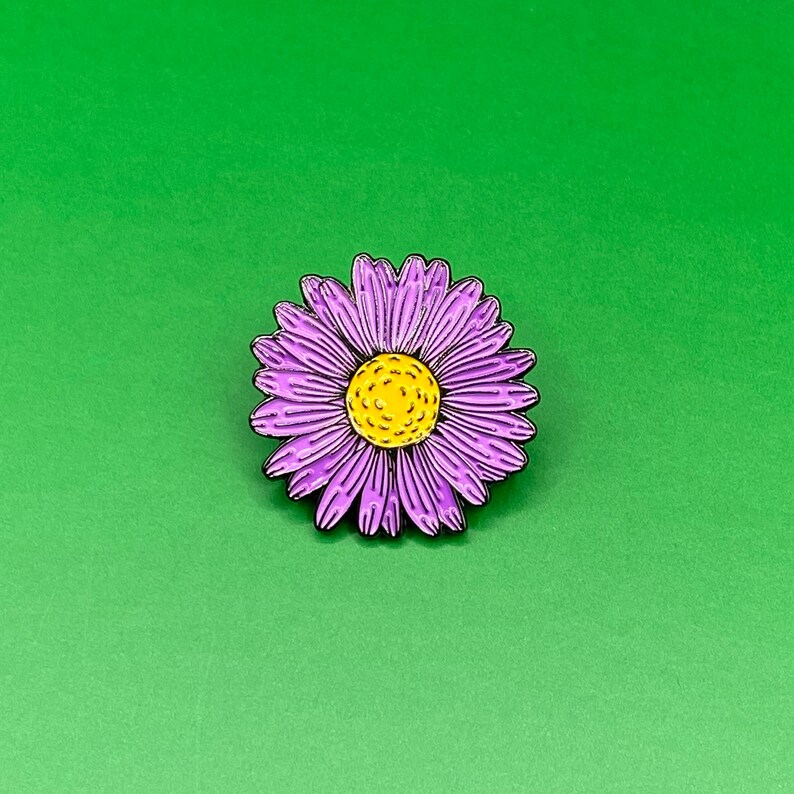 May include: Purple enamel flower pin with a yellow center. The flower has a detailed design and is a great addition to any collection.
