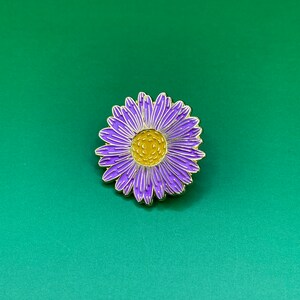 May include: Purple and yellow enamel pin of a flower with a gold outline.