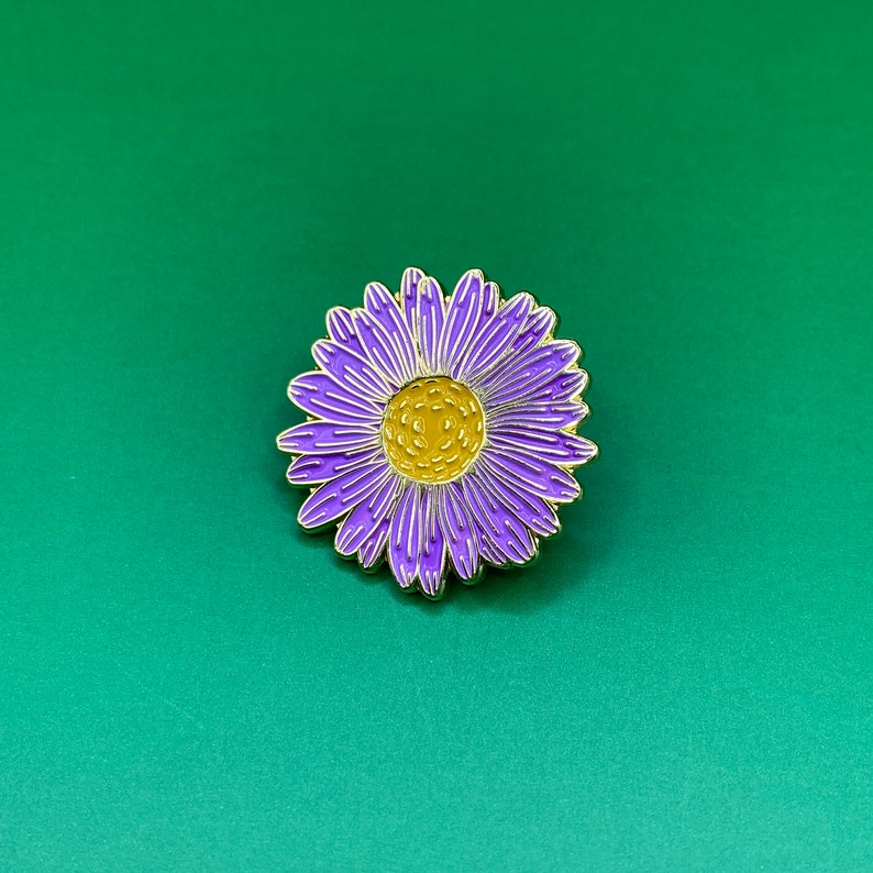 May include: Purple and yellow enamel pin of a flower with a gold outline.