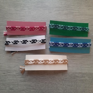 Pode incluir: Cinco pulseiras de amizade com diferentes combinações de cores. As pulseiras são feitas com um padrão de diamante e são exibidas em pequenos cartões.