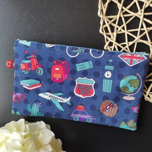 Könnte beinhalten: Eine blaue Reißverschlusstasche mit Reisemotiv. Die Tasche ist mit einem sich wiederholenden Muster von Reise-Icons bedeckt, darunter ein Roller, ein Globus, ein Flugzeug, ein Rucksack, ein Straßenschild mit der Aufschrift "Road Trip" und ein Ticket.