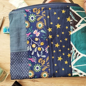 Könnte beinhalten: Eine blaue Patchwork-Kosmetiktasche mit Reißverschluss, mit einem Blumenmuster, einem Sternenmuster und einem grün-weißen Muster. Die Tasche ist aus Stoff und hat einen Reißverschluss.