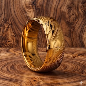 Op de afbeelding: Een gouden ring met een ingewikkeld geëtst ontwerp. De ring heeft een getextureerde buitenband en een gedetailleerd patroon op de voorkant. De ring wordt gepresenteerd op een houten oppervlak, dat de reflecterende, gepolijste afwerking laat zien.