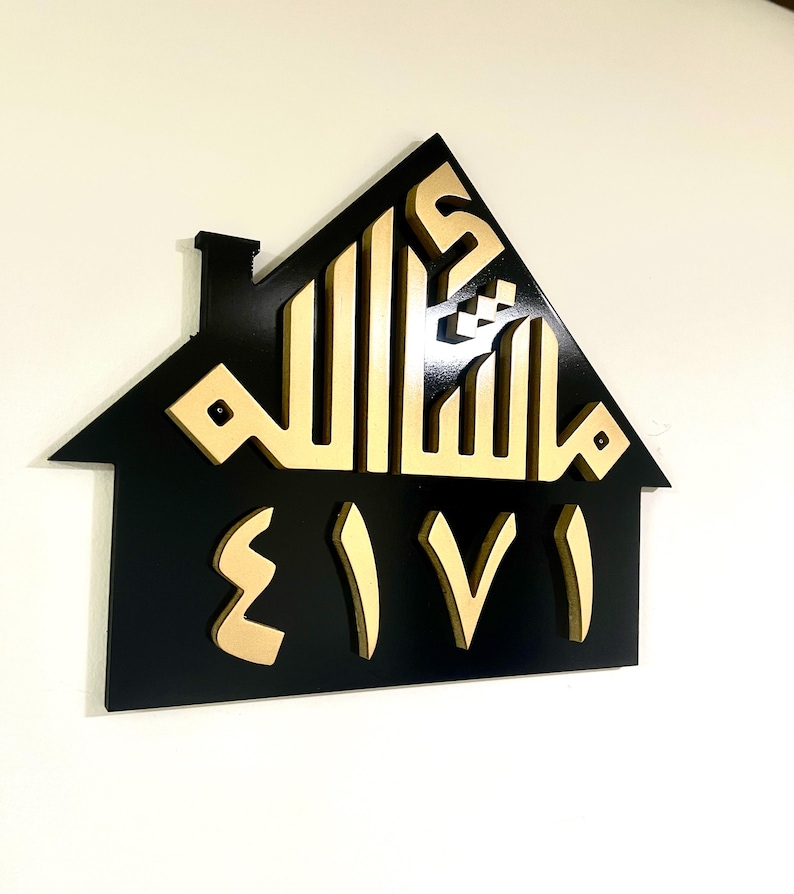 May include: A black house-shaped sign with a gold Arabic inscription and the word "EIVI" in gold letters.