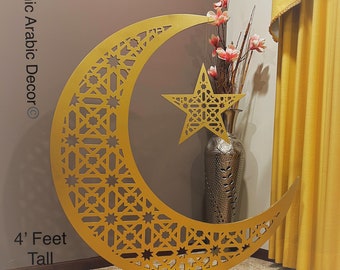 May include: A gold metal crescent moon and star cutout with intricate geometric designs. The cutout is 1.2 metres tall and stands on a round base.  Islamic Arabic Decor.