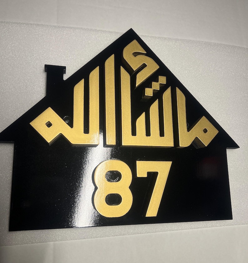 May include: Black house-shaped sign with gold Arabic calligraphy and the number 87.