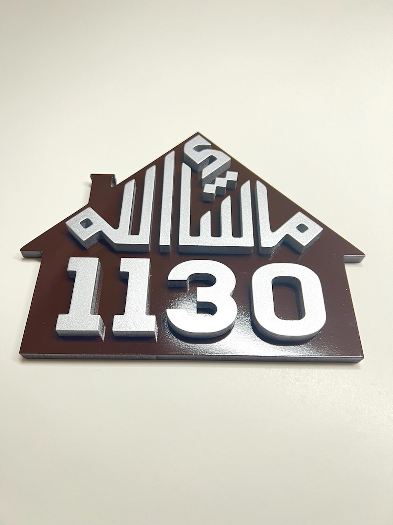 May include: A brown house-shaped sign with a silver Arabic inscription and the number 1130 in silver.