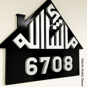 May include: Black house-shaped sign with a silver Arabic calligraphy design and the number 6708 in silver. The sign is made of wood and has a glossy finish. The text "Islamic Arabic Decor&reg;" is in the bottom right corner.