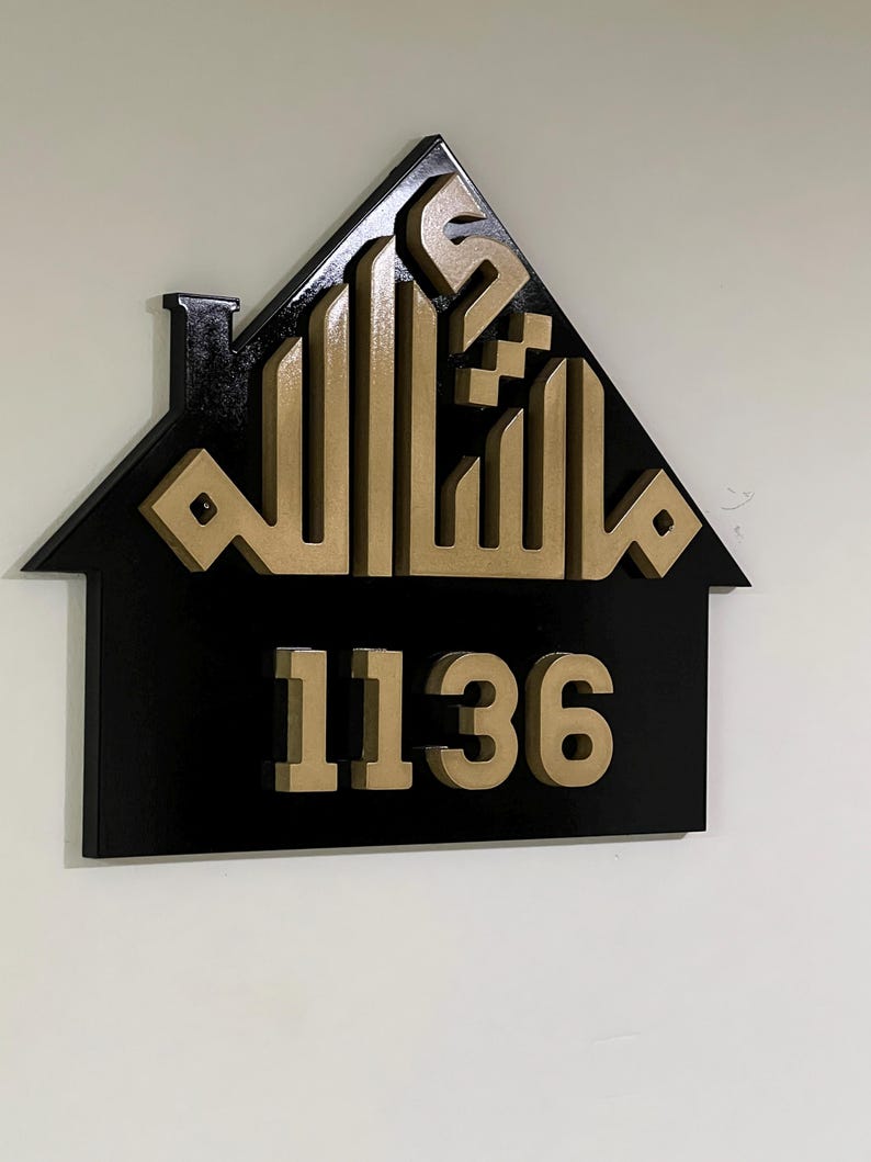 May include: A black house-shaped sign with gold Arabic calligraphy and the number 1136.