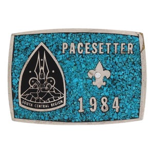 May include: Rectangular belt buckle with a turquoise inlay and silver-colored trim. The buckle features the word "PACESETTER" and the year "1984". A black emblem with the words "SOUTH CENTRAL REGION" is on the left. A scout emblem is on the right.