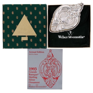 May include: A silver Christmas ornament in the shape of a heart with intricate details. The ornament is in its original box with a green background and a gold Christmas tree. The box also includes a small card with the text "1993 Grande Baroque Sterling Silver Ornament by Wallace Silversmiths."
