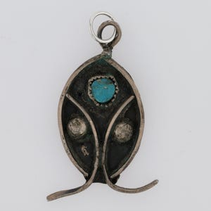 May include: A silver pendant featuring a turquoise stone set in the centre. The pendant has a decorative design with two smaller turquoise stones on either side of the centre stone.