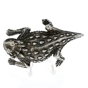 May include: A silver-toned, detailed sculpture of a horned lizard, with a textured, spiky surface. The lizard is curled up in a defensive posture, with its head tucked in and its tail curled around its body.