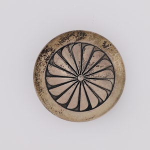 May include: A silver circular pendant with a geometric design of a sunburst with a central dot. The pendant has a slightly aged patina.