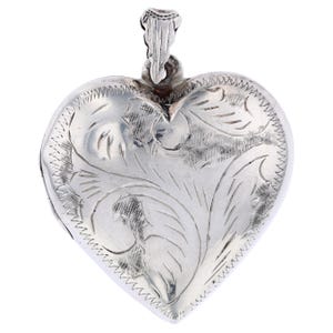 May include: A silver heart-shaped locket with an intricate floral design. The locket has a hinged opening and a loop at the top for attaching a chain.