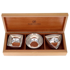 May include: A wooden box with three silver serving bowls of different geometric shapes. The bowls are a square, a circle, and a triangle. The box is branded with the name "PAMPALONI" on the inside of the lid.