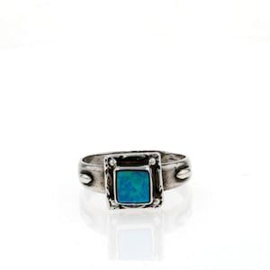 May include: A silver ring with a square blue opal stone set in a silver frame. The ring has a textured band with small silver accents.
