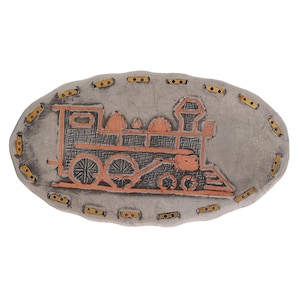 May include: Oval-shaped, silver-toned metal belt buckle featuring a copper-colored train design. The train has detailed wheels and a smokestack. The buckle's border is adorned with gold-colored rivets, creating a vintage aesthetic.
