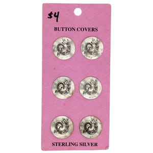 May include: A pink card with the text "$4 BUTTON COVERS STERLING SILVER" printed on it. Six silver button covers with a stylized lizard design are displayed on the card.