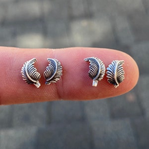 Op de afbeelding: Vier zilveren oorbelletjes in de vorm van een blad op een vinger.