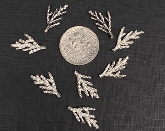 May include: Ten silver-coloured metal sprigs, each resembling a small pine branch, are arranged in a circle around a US dime. The sprigs are approximately the size of the dime.