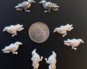 May include: Eight silver-toned crow charms, each with a detailed design. The charms are approximately the size of a US dime.