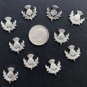 以下が含まれることがあります： アザミの花の形をした銀色の金属製チャームが10個。チャームはアメリカの10セント硬貨と同じくらいの大きさです。