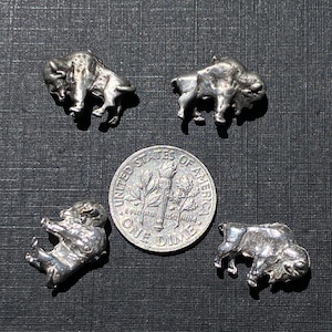 May include: Four silver buffalo charms, each depicting a buffalo in a different pose. The charms are about the size of a ten pence piece.