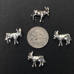 May include: Four silver donkey figurines, each about the size of a US dime. The donkeys are standing on a dark gray surface.