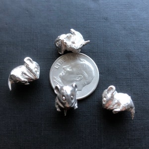 Könnte beinhalten: Vier silberne Mäusefiguren aus Metall, jede in einer anderen Pose, sind auf einer dunkelgrauen Oberfläche angeordnet. Eine silberne US-Dime-Münze befindet sich in der Mitte der Anordnung.