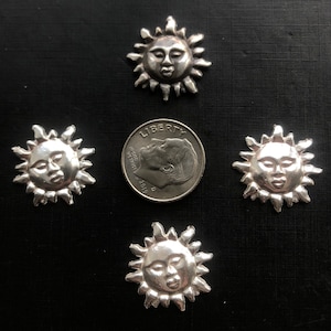 May include: Four silver sun charms with a face on each. The charms are about the size of a US dime.