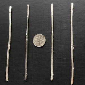 May include: Four silver-colored metal sticks with a textured, twig-like appearance are arranged on a black surface. A dime is placed near the center for size comparison. The sticks vary slightly in length and detail.