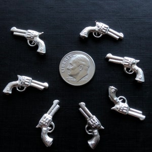 May include: Seven silver-colored miniature revolver toy guns arranged in a circle around a silver US dime coin. The coin is dated 2002.