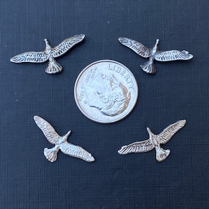 May include: Four silver metal seagull charms, each about the size of a UK 20 pence coin, arranged in a circle around a US quarter.