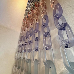 May include: A decorative wall hanging composed of multiple vertical strands of interlocking oval links made from translucent acrylic. The links feature a gradient color transition, shifting from clear and frosted tones to shades of purple, pink, and blue.