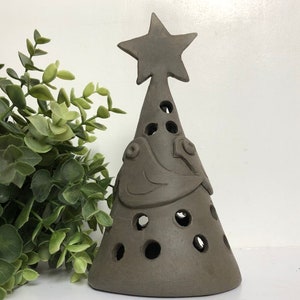 Op de afbeelding: Een bruine keramische kerstboom met een ster bovenop en uitsnijdingen van vogels. De boom heeft gaten aan de zijkanten.