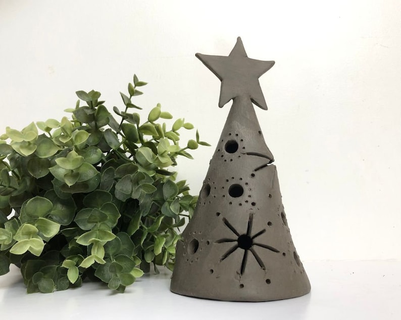 Op de afbeelding: Een bruine keramische kerstboomversiering met een ster bovenop en uitgesneden ontwerpen. De boom is versierd met kleine cirkels en een grotere stervorm.