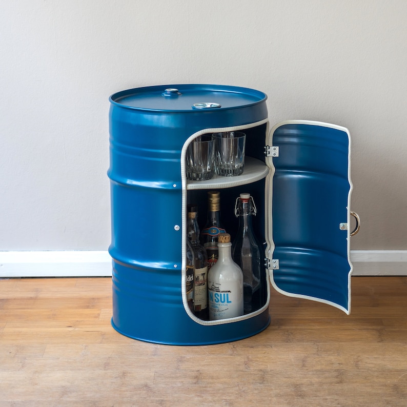 Puede incluir: Un barril de metal azul reconvertido en un armario de bar con una puerta que se abre para revelar estantes para guardar botellas y vasos.