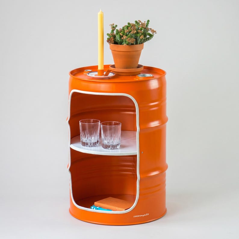 May include: An orange metal barrel repurposed as a side table. It features a white interior with two shelves, holding two glasses and an orange book. A small potted plant and a yellow candle sit on top. The barrel has a white trim.