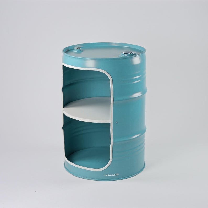 May include: A teal metal barrel-shaped shelf unit with two white shelves. The unit has a rounded rectangular opening on the front. The barrel has a ridged texture and a white trim around the opening. The bottom of the unit has the text "JochenHeist".