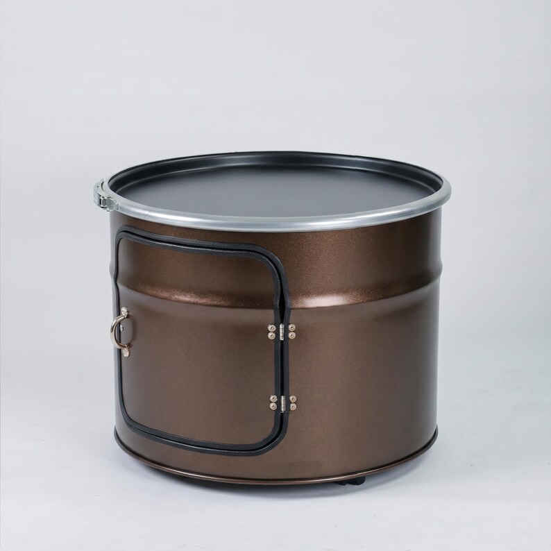 Puede incluir: Una unidad de almacenamiento cil&iacute;ndrica de metal con acabado en color bronce met&aacute;lico. Presenta una parte superior plana negra bordeada por una banda de metal plateado y una puerta lateral rectangular con un peque&ntilde;o tirador plateado y bisagras.