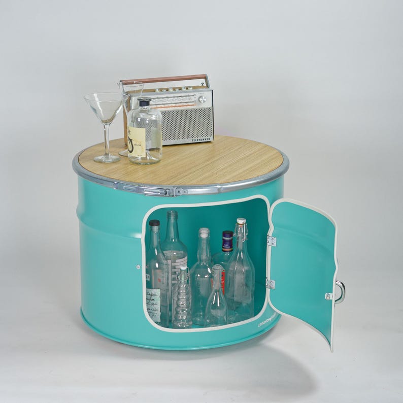 Puede incluir: Un mueble de tambor met&aacute;lico de color turquesa con una tapa circular de madera clara y una puerta abatible. El interior contiene varias botellas de vidrio transparente. Encima hay una radio de estilo vintage, una botella y una copa de martini.