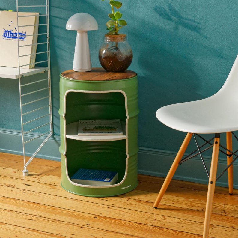 May include: A green metal side table made from a repurposed barrel, featuring a wooden top and two interior shelves. A white mushroom-shaped lamp and a glass jar with a plant sit on top. The table is 24 inches tall.