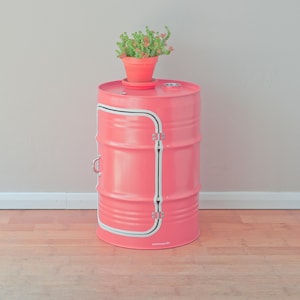 Puede incluir: Un barril de metal rosa con un dise&ntilde;o de rayas blancas se ha reutilizado como mesa auxiliar. Una peque&ntilde;a planta suculenta en maceta se coloca encima de la mesa.